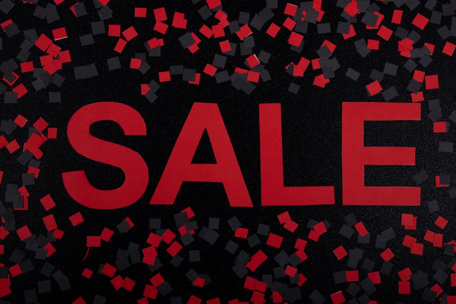 A red rectangular sale sign with bold white capital letters spelling 'SALE' is positioned on a wooden floor beneath a glass display case. The sign is slightly crumpled around the edges and partly tuck